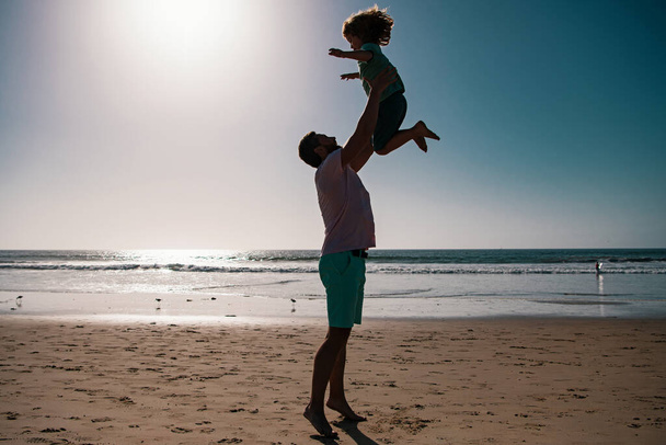 Father throws son up against the blue sky. Dad throwing child, silhouette on sunset. Concept of friendly family and of summer vacation - Foto, Imagen