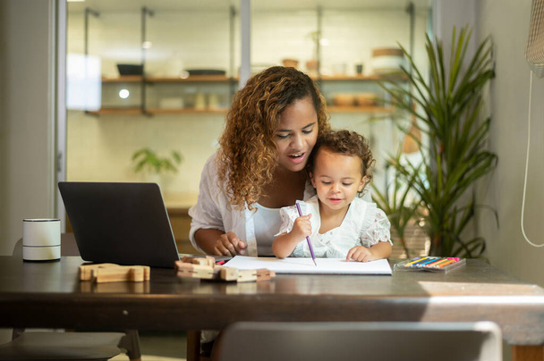 African American mother wearing casual clothes working in her home while daughter playing  or education  - Foto, imagen