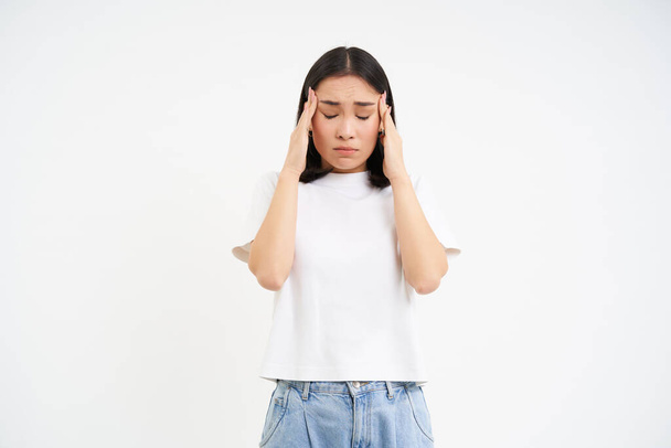 Traurige Frau hält Hände auf den Kopf, leidet an Kopfschmerzen, hat Migräne, fühlt sich schwindelig, steht vor weißem Hintergrund. - Foto, Bild