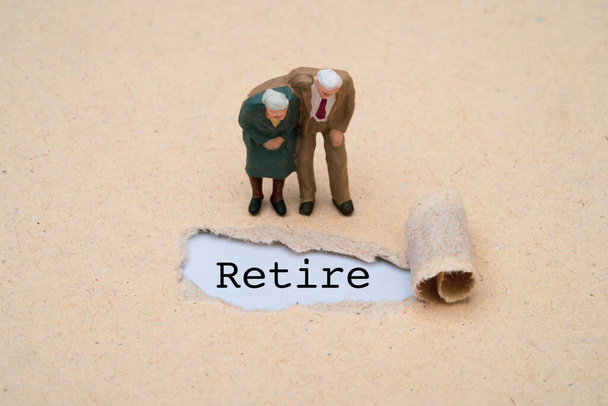Couple miniature figure senior pensioners man and woman standing with retire wording on brown punch paper for wealth financial planning ,money saving and life insurance of retirement concept.  - Photo, Image