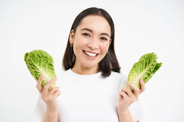 Happy korean woman vegetarian, smiling and showing cabbage, eating lettuce on diet, leads active lifestyle, white background. - Photo, image