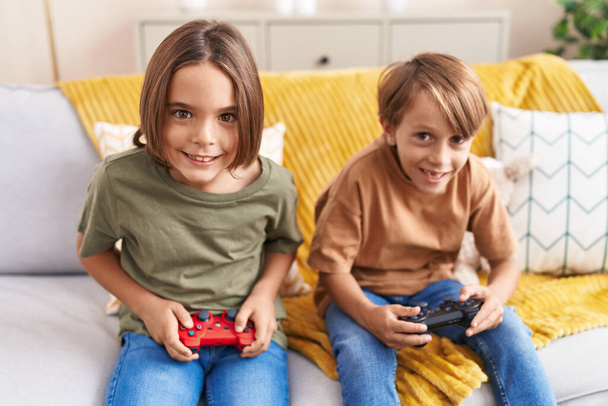 Adorable boys playing video game sitting on sofa at home - Fotó, kép