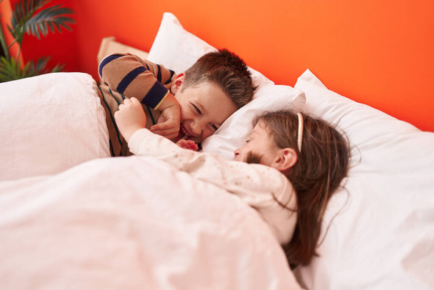 Чарівний хлопчик і дівчинка посміхаються впевнено лежачи в ліжку в спальні
 - Фото, зображення