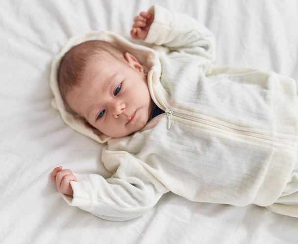 Adorable caucasian baby lying on bed with relaxed expression at bedroom - Foto, Imagen