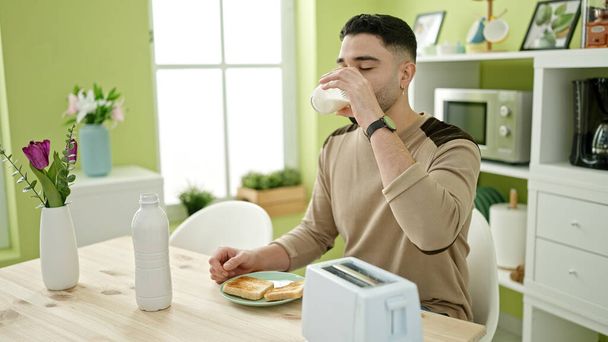 Fiatal arab férfi iszik pohár tejet ül az asztalon otthon - Fotó, kép
