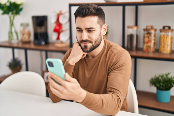 Young hispanic man using smartphone sitting on table at home - Photo, Image