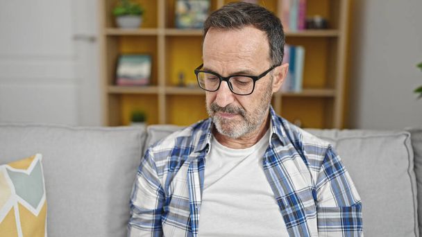 Middle age man sitting on sofa with relaxed expression at home - Photo, Image