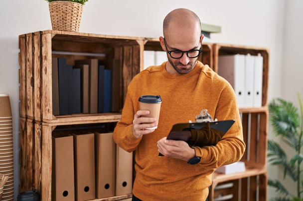 Junger Mann trinkt Kaffee und hält Klemmbrett im Büro - Foto, Bild