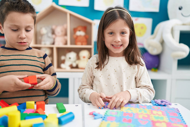 Очаровательный мальчик и девочка играют со строительными блоками и словарной головоломкой в детском саду - Фото, изображение