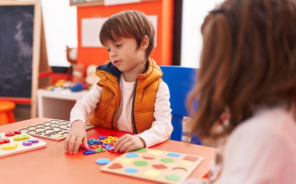Adorable caucasian boy playing with maths puzzle game sitting on table at kindergarten - 写真・画像