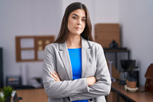 Young beautiful hispanic woman business worker standing with arms crossed gesture at office - Valokuva, kuva