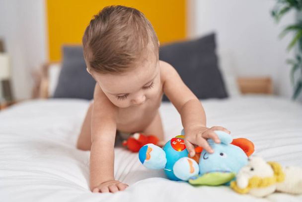 Adorável bebê caucasiano brincando com elefante brinquedo sentado na cama no quarto - Foto, Imagem