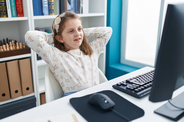 Adorable blonde girl student using computer resting with hands on head at classroom - Photo, Image