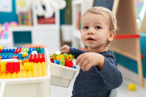 Adorable blond toddler playing with construction blocks standing at kindergarten - Foto, imagen