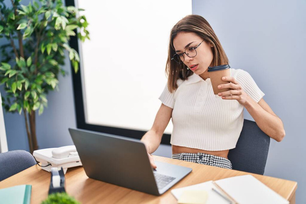 Молода красива іспанська жінка бізнесмен використовує ноутбук п'є каву в офісі
 - Фото, зображення