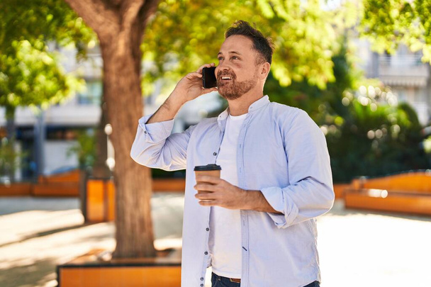 Jeune homme caucasien parlant sur le smartphone boire du café au parc - Photo, image