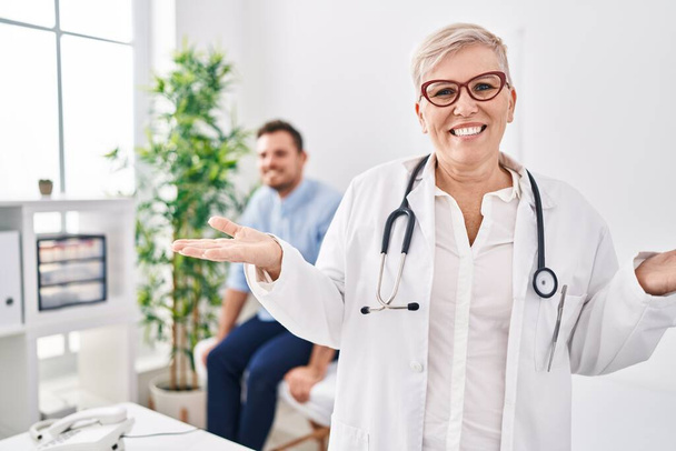 Kobieta lekarz noszący mundur i stetoskop w klinice medycznej świętując osiągnięcie ze szczęśliwym uśmiechem i ekspresją zwycięzcy z podniesioną ręką  - Zdjęcie, obraz