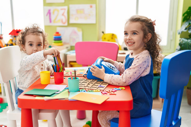 Adorable girls playing telephone toy sitting on table at kindergarten - Foto, imagen