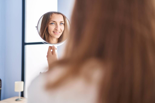Молодая женщина улыбается доверчиво глядя на зеркало в спальню - Фото, изображение