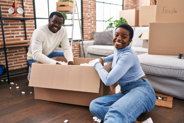 mężczyzna i kobieta para unboxing kartonowe pudełko siedzi na podłodze w nowym domu - Zdjęcie, obraz