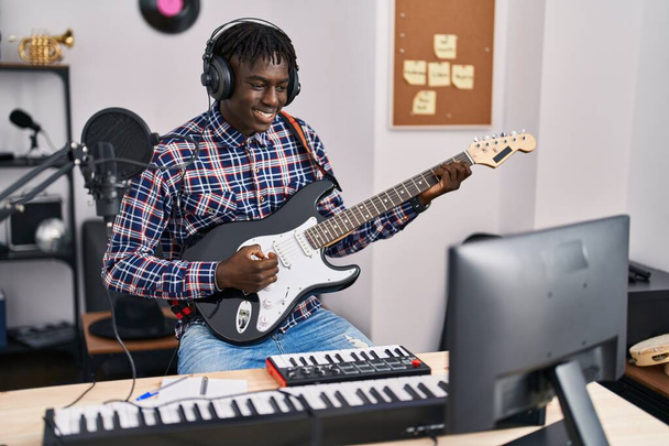 Αφροαμερικάνος μουσικός χαμογελαστός με αυτοπεποίθηση παίζοντας ηλεκτρική κιθάρα στο στούντιο μουσικής - Φωτογραφία, εικόνα