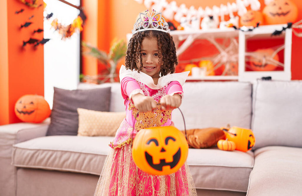 menina afro-americana vestindo fantasia princesa segurando cesta de abóbora em casa - Foto, Imagem