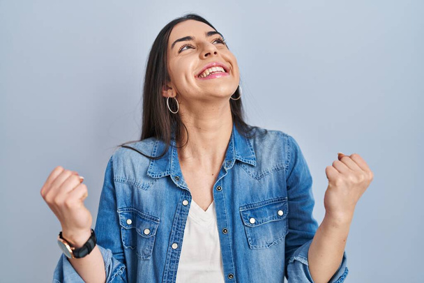 Hispanic woman standing over blue background celebrating surprised and amazed for success with arms raised and eyes closed. winner concept.  - Photo, Image