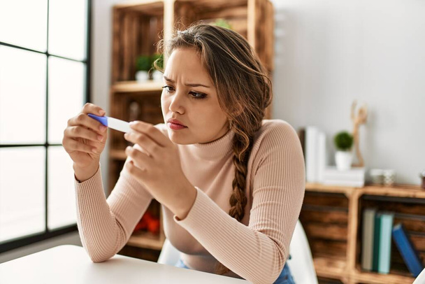Молода красива іспаномовна жінка тримає тест на вагітність, сидячи на столі вдома
 - Фото, зображення