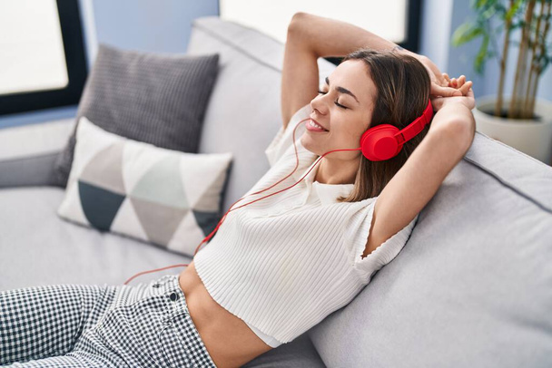 Young beautiful hispanic woman listening to music relaxed on sofa at home - Foto, afbeelding