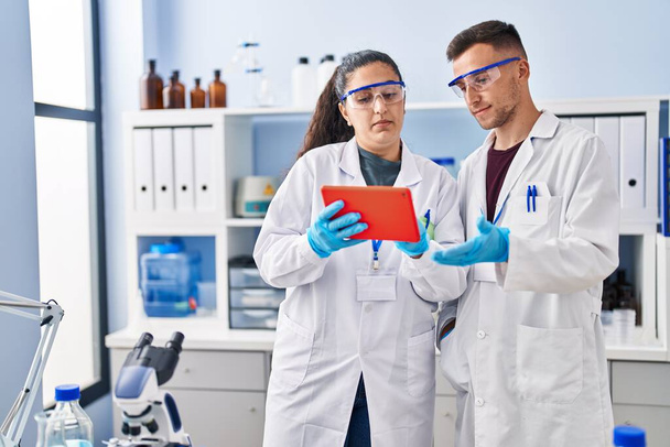 Férfi és nő, akik tudományos egyenruhát viselnek, érintőpadot használnak a laborban. - Fotó, kép