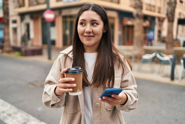 Young hispanic woman using smartphone drinking coffee at street - Zdjęcie, obraz