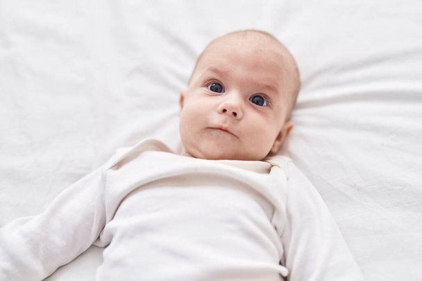 Adorable caucasian baby lying on bed with relaxed expression at bedroom - Foto, afbeelding