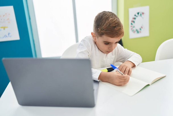 Adorable hispanic boy student using laptop writing notes at classroom - Foto, Imagem