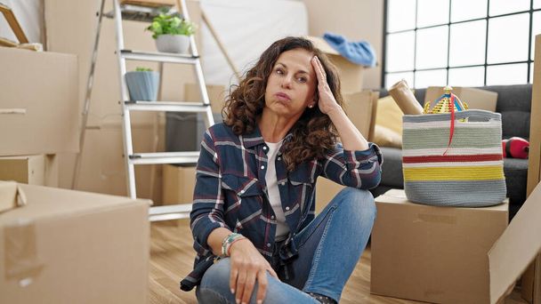 Middle age hispanic woman sitting on floor looking upset at new home - Foto, immagini