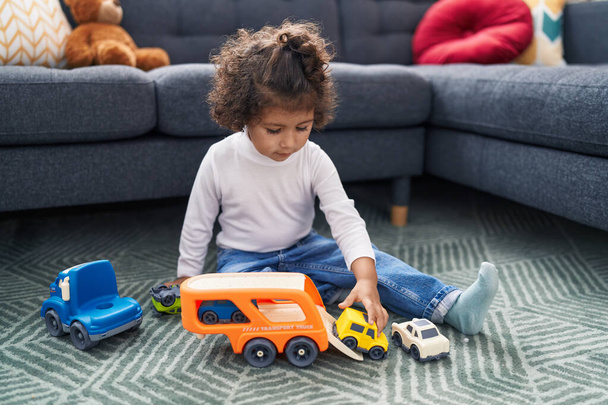 Adorable hispanic girl playing with car toy sitting on floor at home - Foto, Bild