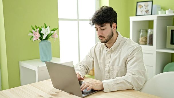 Fiatal spanyol férfi laptoppal ül az asztalon az ebédlőben - Fotó, kép