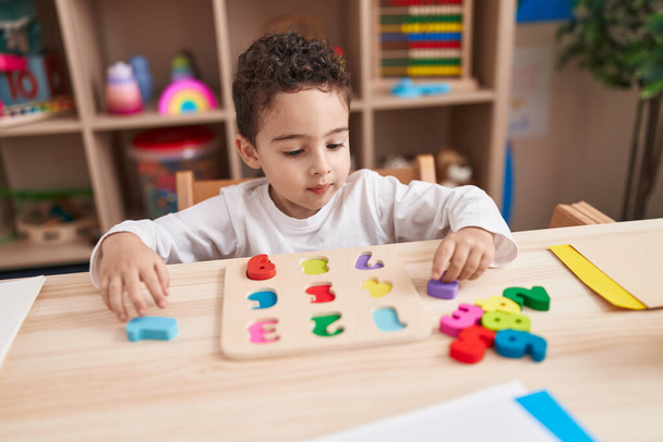 Чарівний іспаномовний хлопчик грає з математичною грою-головоломкою, сидячи на столі в дитячому саду
 - Фото, зображення