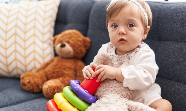 Adorable caucasian baby playing with hoops game sitting on sofa at home - Foto, Bild