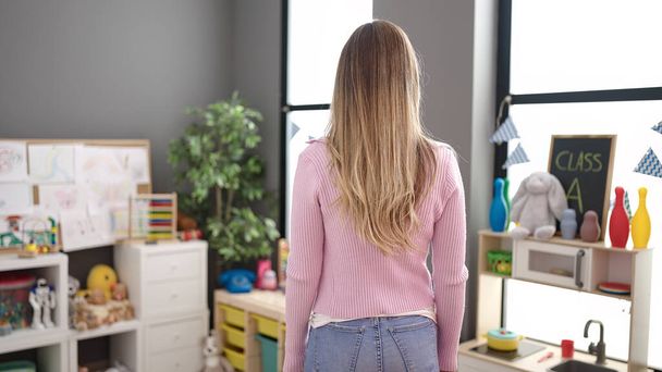 Young blonde woman teacher standing on back view at kindergarten - Foto, immagini
