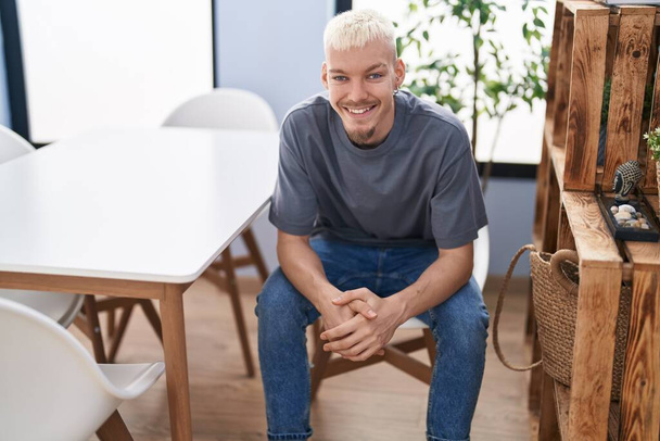 Jeune homme caucasien souriant confiant assis sur une chaise à la maison - Photo, image