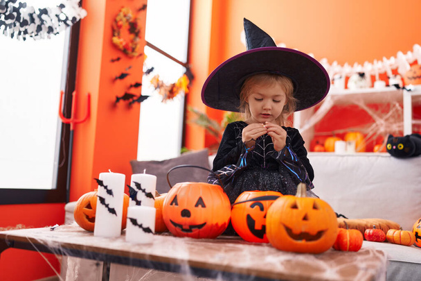 Adorable blonde girl wearing witch costume holding sweets on pumpkin basket at home - Photo, Image