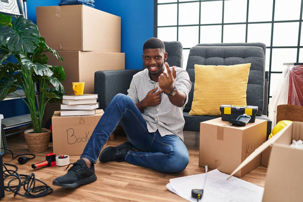 アフリカ系アメリカ人の男に座っている床に新しい家の手招きここに来てジェスチャーで歓迎幸せと笑顔を招待  - 写真・画像