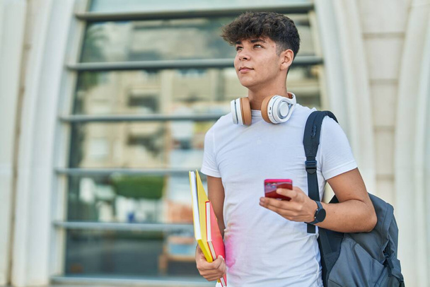 Молодой испаноязычный студент-подросток, использующий смартфон с книгами в университете - Фото, изображение