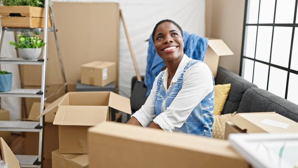 Африканська американка, усміхаючись, впевнено сидить на дивані в новому домі. - Фото, зображення