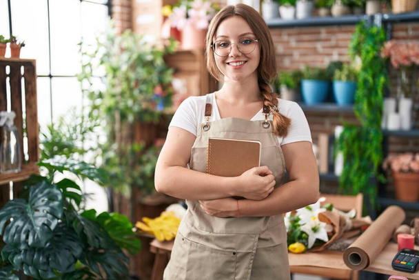 Young blonde woman florist smiling confident holding notebook at florist - Photo, Image