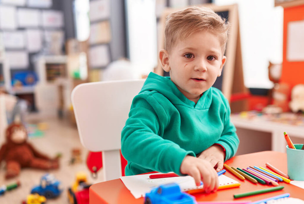 Adorable caucasian boy preschool student sitting on table drawing on notebook at kindergarten - Photo, Image