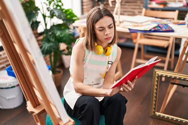 Молода красива іспаномовна жінка художник читає книгу в художній студії
 - Фото, зображення