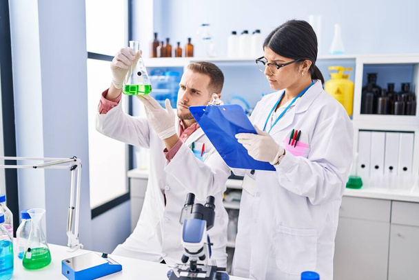 Mann und Frau in Wissenschaftleruniform messen Flüssigkeit im Labor - Foto, Bild