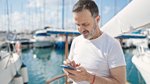 Чоловік середнього віку використовує смартфон з серйозним виразом на човні
 - Фото, зображення