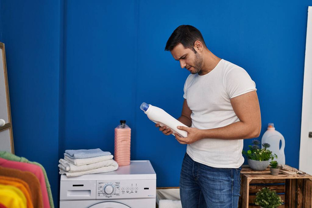 Young hispanic man holding detergent bottle at laundry room - Photo, Image